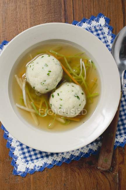 Clear broth with vegetables and dumplings in white plate over towel with spoon — Stock Photo