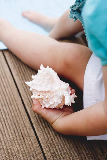 Cropped view of child holding sea shell on edge of swimming pool — Stock Photo