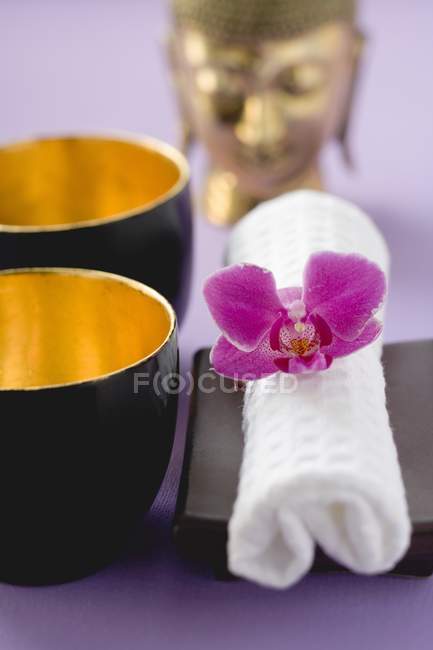 Primo piano vista di due ciotole, asciugamano con fiore orchidea tagliata e statua di Buddha — Foto stock