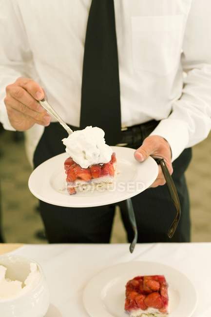 Closeup cropped view of man holding plate with piece of strawberry flan and cream — Stock Photo