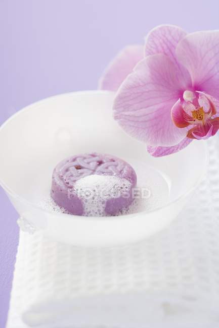 Sabão com espuma em tigela branca na toalha por flor de corte de orquídea — Fotografia de Stock