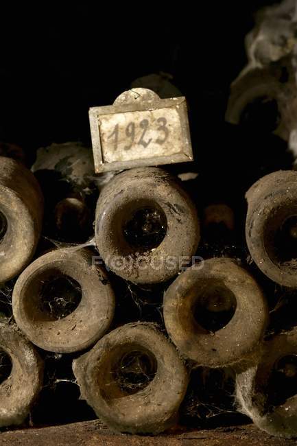 Piled old wine bottles with year tag and dust in wine cellar — Stock Photo