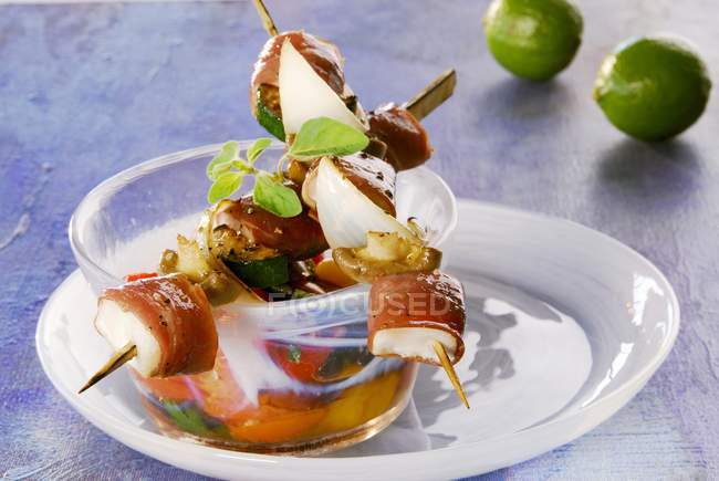 Forellenspieße mit Pilzen und Zwiebeln auf weißem Teller mit Glasschale über Tisch — Stockfoto