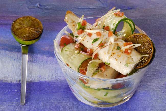 Fried trout fillet on tomato and cucumber salad in glass bowl over blue surface — Stock Photo