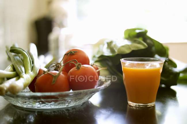 Glass of juice beside dish of vegetables — Stock Photo