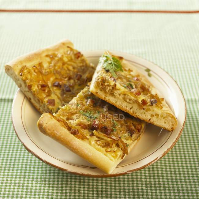 Three pieces of onion tart on a plate over green surface — Stock Photo