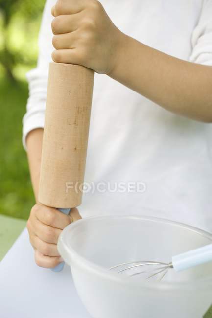 Vue recadrée des mains de l'enfant tenant le rouleau à pâtisserie par bol et fouet — Photo de stock