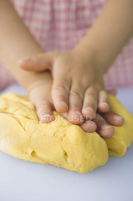 Vue rapprochée des mains de l'enfant pétrissant la pâte — Photo de stock