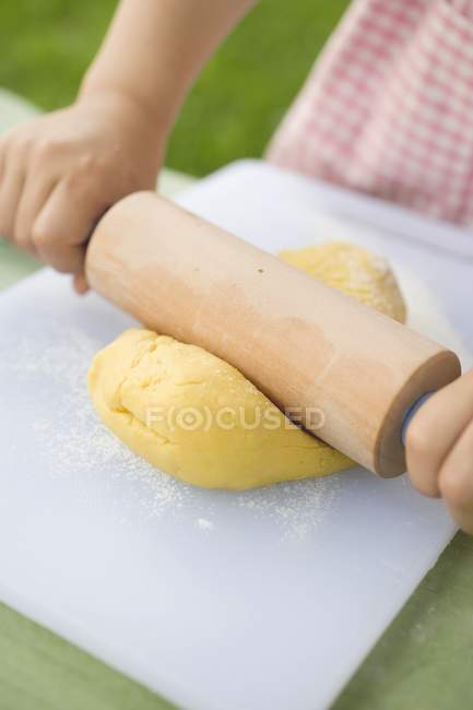 Vue recadrée de l'enfant déroulant la pâte — Photo de stock