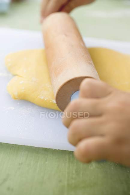 Вид крупным планом на ребенка, прокатывающего тесто — стоковое фото