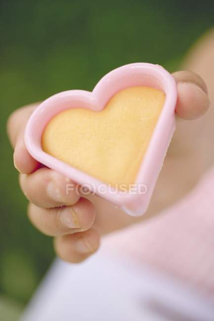 Closeup view of child hand holding cut-out heart-shaped biscuit — Stock Photo