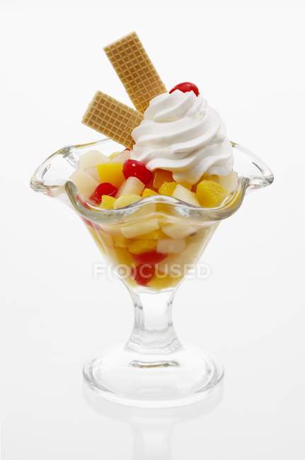 Closeup view of fruit cocktail with cream and wafers in glass on white surface — Stock Photo