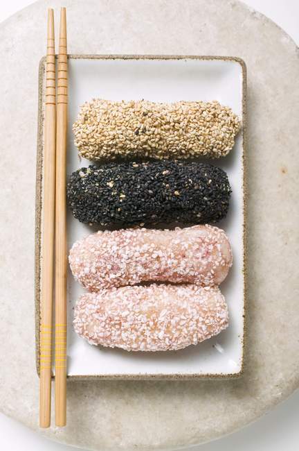 Closeup top view of dumplings coated in sesame seeds and coconut flakes with chopsticks on rectangular plate — Stock Photo
