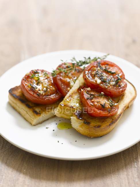 Toast topped with tomatoes and thyme on white plate — Stock Photo