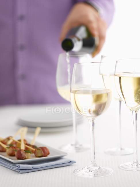 Cropped view of person pouring white wine in glasses — Stock Photo