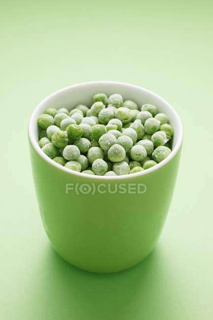 Guisantes congelados en taza verde - foto de stock