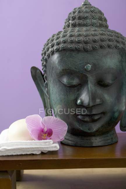 Orquídea flor y jabón bar en toalla blanca al lado de la estatua de Buda - foto de stock