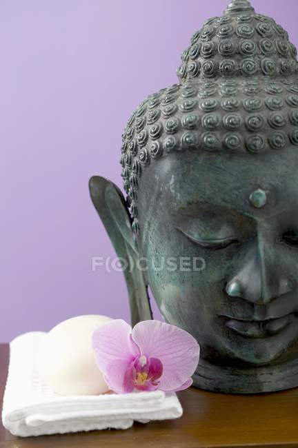 Barre de savon et fleur d'orchidée sur serviette blanche à côté de la statue de Bouddha — Photo de stock