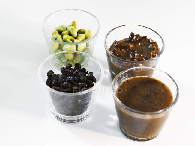 Sojabohnen und Sojabohnensaucen in Gläsern auf weißer Oberfläche — Stockfoto