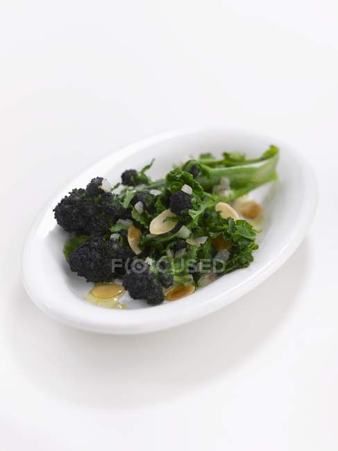 Broccoli with slivered almonds on white plate over white surface — Stock Photo