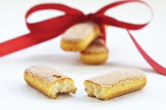 Closeup view of sponge fingers with a red bow on white surface — Stock Photo