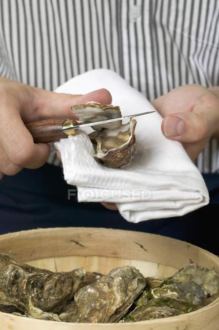 Cropped view of man opening oyster with knife on cloth — Stock Photo