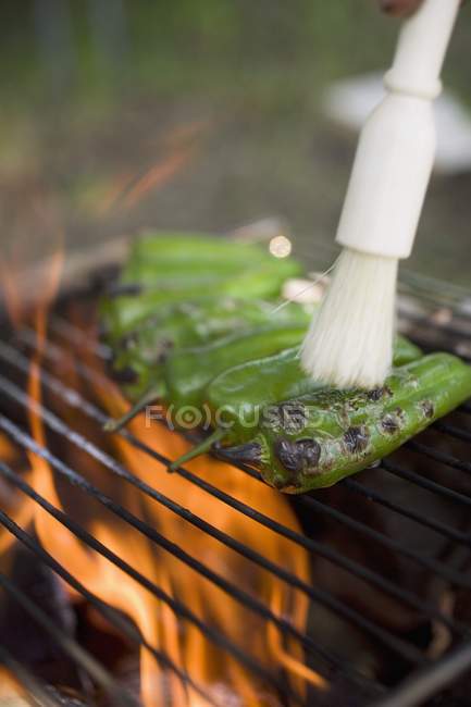 Green chillies on barbecue grill rack with brush — Stock Photo