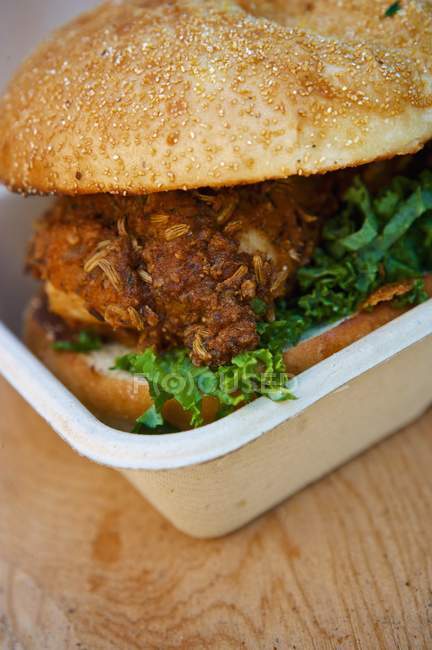 Смажений курячий бутерброд з листям на булочці над дерев'яною поверхнею — стокове фото