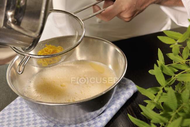 Closeup cropped view of person straining reduced orange syrup through a sieve — Stock Photo