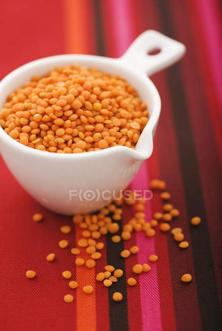 Vista close-up de lentilhas vermelhas em um copo de medição branco — Fotografia de Stock