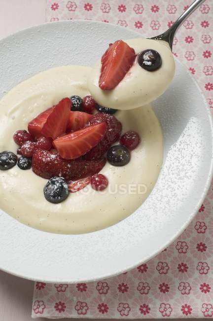 Closeup view of vanilla cream with berries on spoon and plate — Stock Photo
