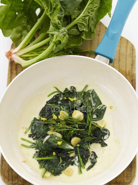 Сливочный шпинат с чесночными крышками в сковороде; сверху и свежий шпинат — стоковое фото