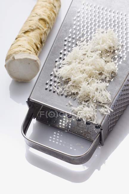 Horseradish, whole and grated with a grater on white background — Stock Photo