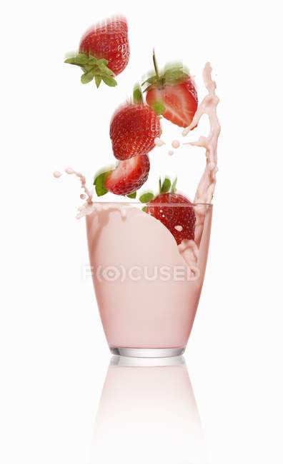 Fresas que caen en un vaso de leche - foto de stock