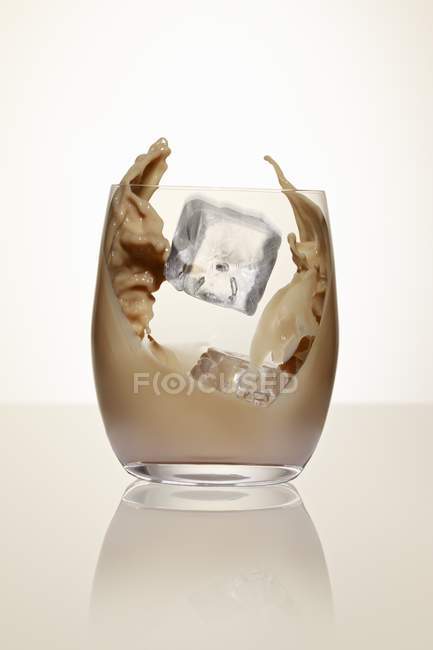 Closeup view of ice cubes falling to glass of cream liqueur — Stock Photo