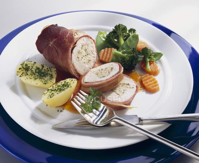 Stuffed ham-wrapped chicken breast with vegetables on platter with cutlery — Stock Photo