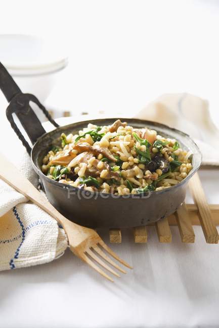 Wheat with spinach and dried mushrooms in pot over wooden stand — Stock Photo
