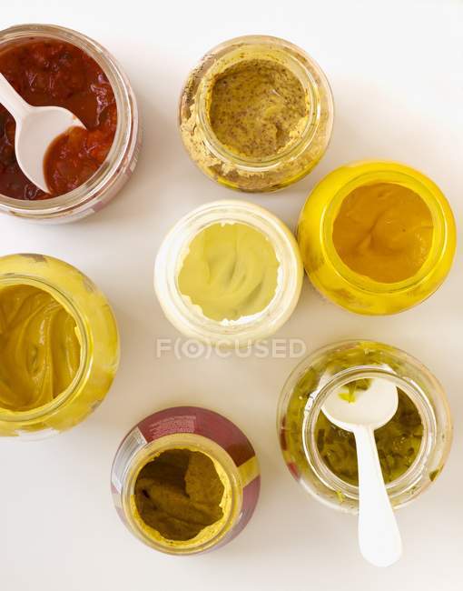 Vue de dessus de pots de condiments ouverts assortis avec moutarde, mayonnaise, salsa et savourer — Photo de stock
