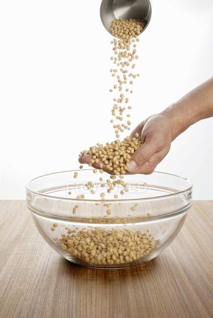 Mãos derramando grãos de soja em tigela — Fotografia de Stock