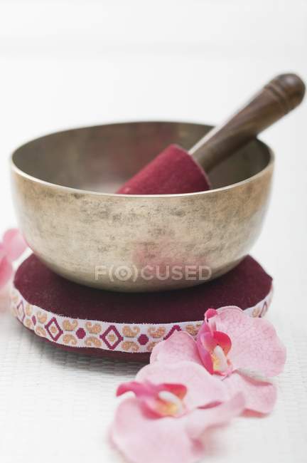 Vue rapprochée d'un bol chantant sur un oreiller près d'orchidées roses — Photo de stock