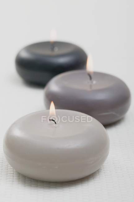 Closeup view of three burning floating candles on white surface — Stock Photo