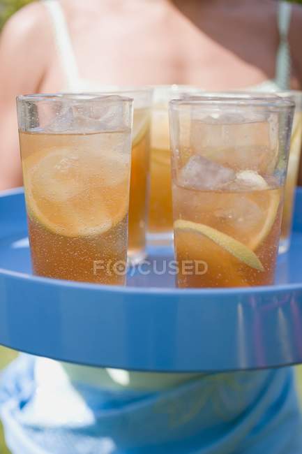 Крупный план холодного чая в стаканах на подносе с женщиной на заднем плане — стоковое фото