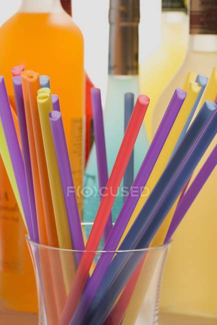 Pajitas coloridas para beber en un vaso cerca de botellas con diferentes bebidas - foto de stock