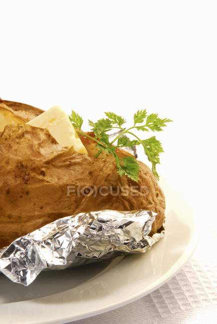 Baked potato with butter and chervil in foil — Stock Photo