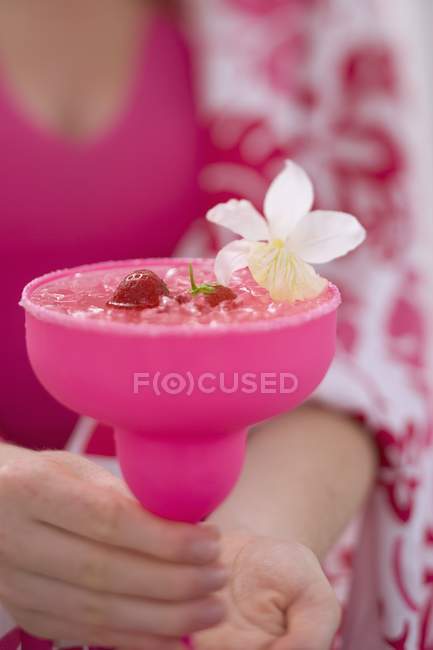 Primer plano vista recortada de la mujer sosteniendo bebida con fresas y flores - foto de stock