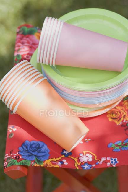 Tazas de papel de colores y platos en taburete plegable en el jardín - foto de stock