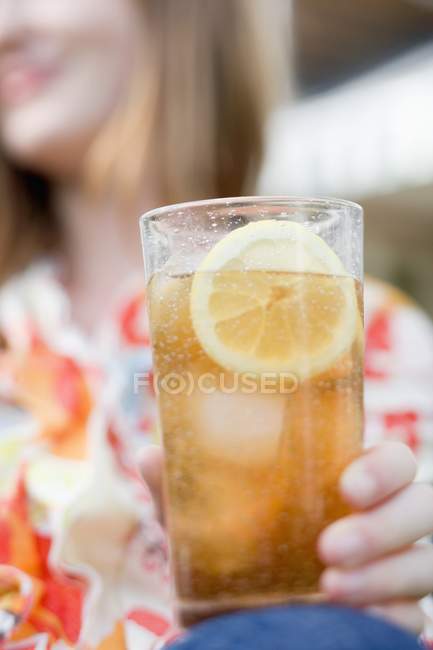 Closeup view of woman holding glass of iced tea with lemon slice — Stock Photo