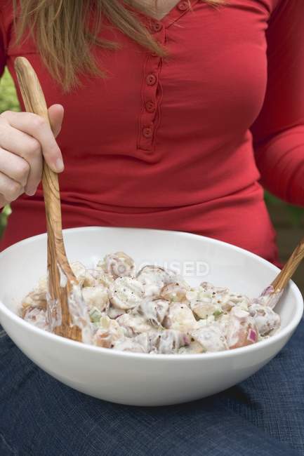 Mujer mezclando ensalada de papa con servidores de ensalada - foto de stock