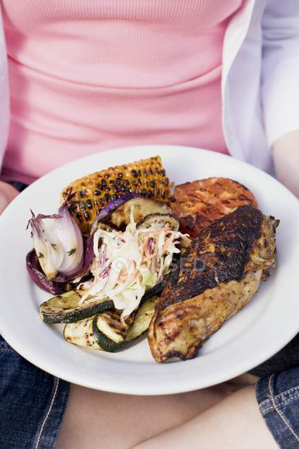 Woman holding plate of grilled chicken — Stock Photo