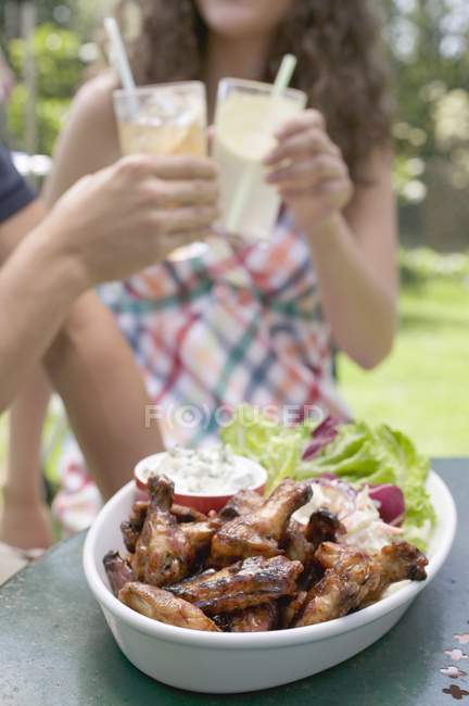 Денний вид на курячі крильця на грилі з салатом і людьми на фоні — стокове фото